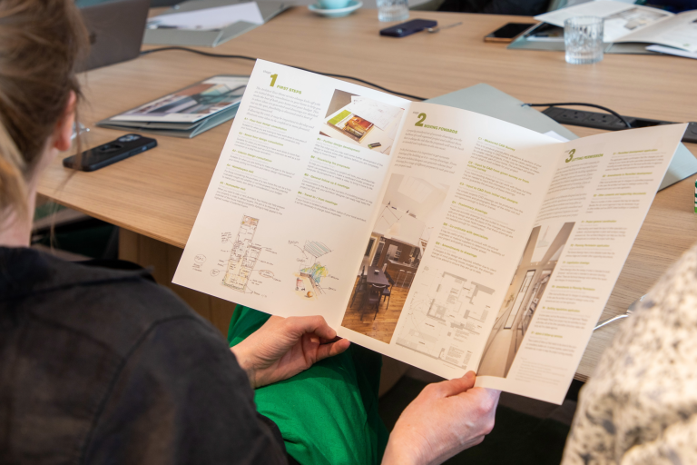 Customer holding and reviewing the Architect Your Home printed service menu, outlining design, survey, planning, and project support stages.