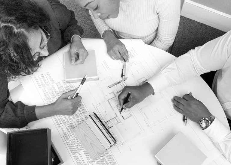 Architect and clients reviewing building plans and materials during the builder selection stage of a home renovation project.