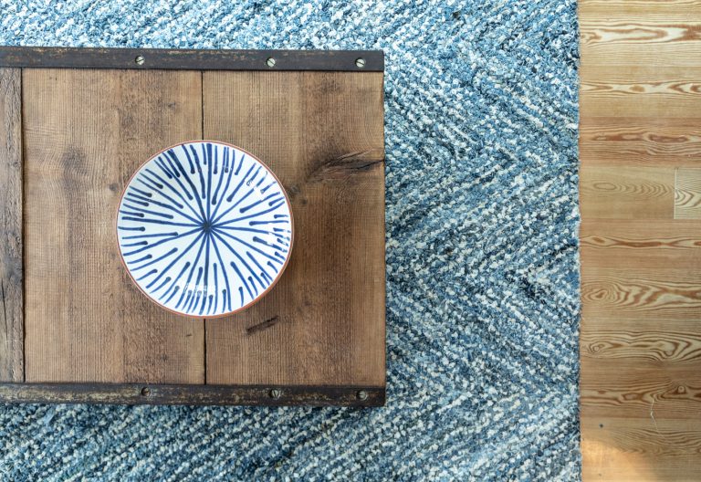 Wooden coffee table with decorative ceramic plate and blue woven rug on timber floor - home staging detail.