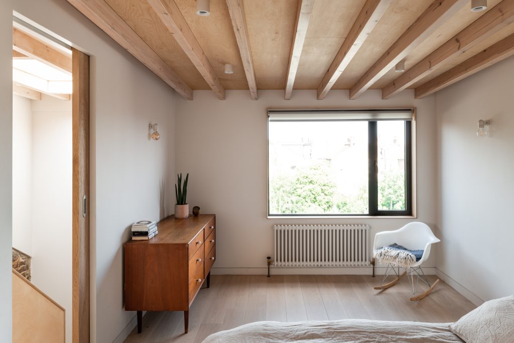 Loft bedroom with large window, white walls and timber ceiling beams
