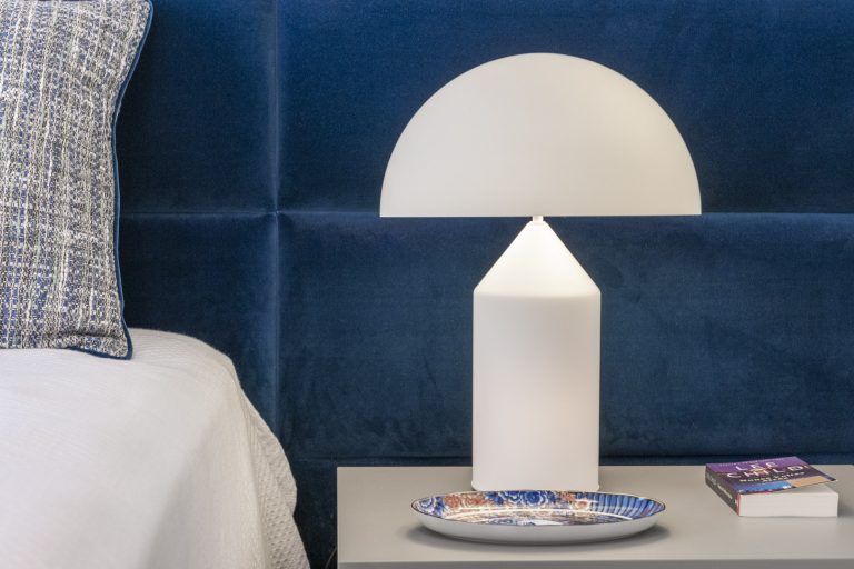 Styled bedside detail with sculptural lamp, velvet headboard, and decorative tray - reflecting the refinement and finish that elevate a completed scheme.