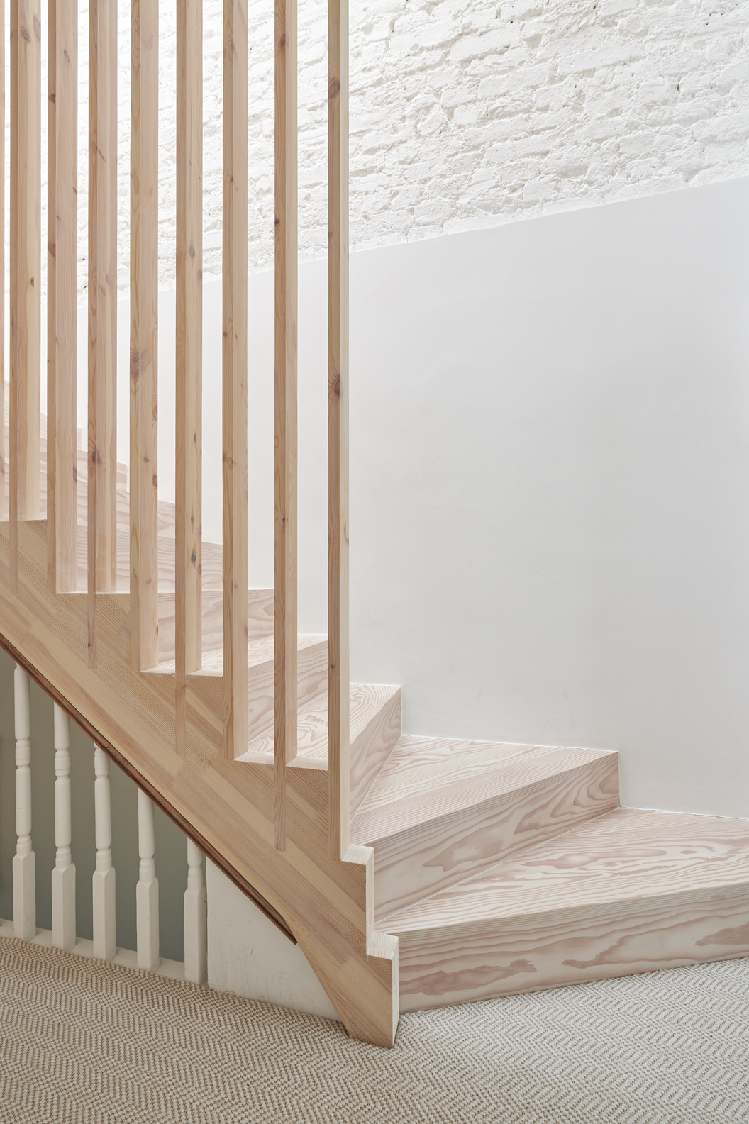Detail of a loft conversion staircase with natural timber treads, vertical slatted balustrade, and exposed white brick wall.